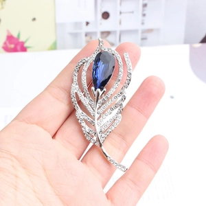 Close-up of feather brooch with blue teardrop crystal and sparkling micro-inlaid stones