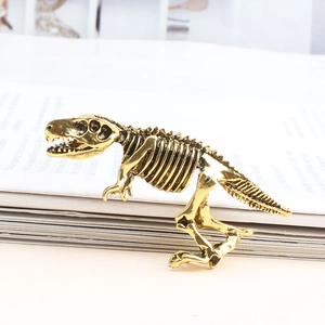 Vue détaillée d'une broche squelette de Tyrannosaure en alliage doré posée sur un livre