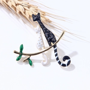 Broche créative en émail avec chats noir et blanc sur une branche dorée et feuilles vertes