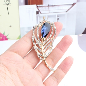 Macro shot of gold feather brooch with a dark blue teardrop gem and sparkling crystals