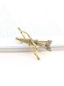 Vue détaillée d'une broche arc et flèche dorée vintage avec cristaux ambrés sur un livre