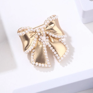 Elegant gold bow brooch with white faux pearls on a minimalist white platform