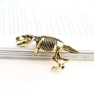 Broche squelette de dinosaure en or antique sur fond de magazine blanc