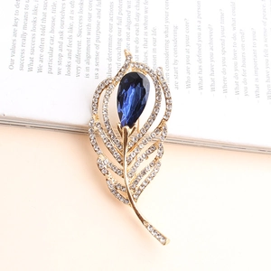 Elegant gold feather brooch with blue pear-shaped gemstone and white crystals