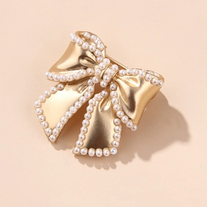 Creative gold bow brooch with white pearls in a retro style on warm beige background