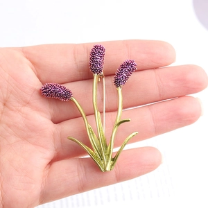 Detail of flower pin with purple petals and golden stem held by hand for scale