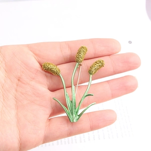 Detail of floral pin brooch featuring golden stalks and green enamel leaves held in hand