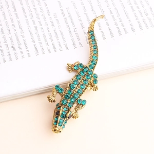Broche crocodile étincelante en cristaux verts sur un livre ouvert avec métal doré