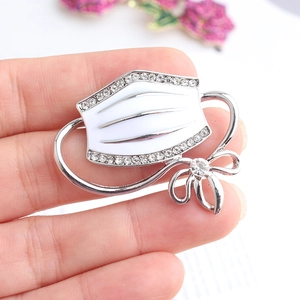 Macro shot of white enamel face mask brooch with sparkling rhinestones and silver bow