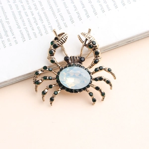 Détail d'une broche crabe vintage dorée avec une opale et des strass verts brillants