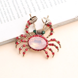 Vue détaillée d'une broche crabe dorée ornée de strass rouges sur fond de magazine anglais