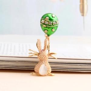Dettaglio di una spilla a forma di coniglio rosa con palloncino smaltato verde e oro