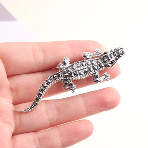 Vue détaillée de la broche crocodile sertie de strass foncés tenue dans la main