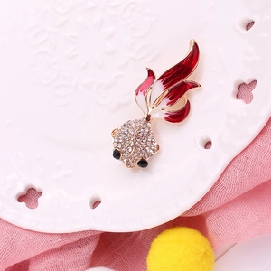 Macro de un broche de pez dorado con pedrería brillante y cola de esmalte rojo en porcelana