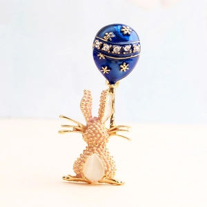 Dettaglio di spilla a coniglio dorato con palloncino blu decorato con strass e opale