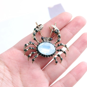 Détail macro d'une broche crabe avec opale et strass verts tenue à la main