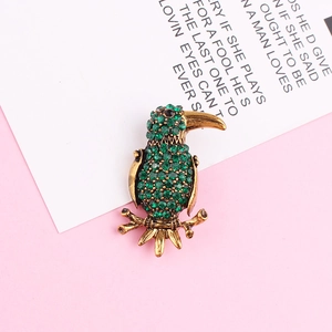 Macro detail of vintage gold bird brooch with green rhinestones and red eye accent