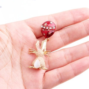 Dettaglio della spilla a coniglio dorato con palloncino rosso smaltato e strass brillanti