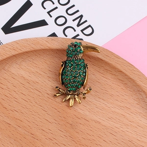 Detailed close-up of a bird brooch featuring green rhinestones and golden branches