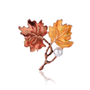 Creative leaf brooch with red and gold enamel leaves and a white pearl on white background