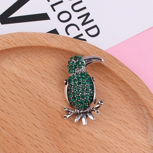 Close-up of a silver bird brooch with green rhinestones perched on a metal branch