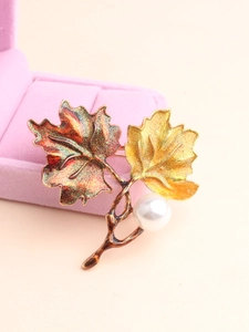 Detail of maple leaf brooch with red and yellow glitter finish and a central white pearl
