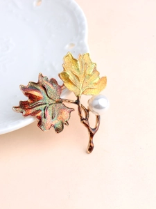 Detail of maple leaf brooch featuring glitter enamel leaves and a round white pearl