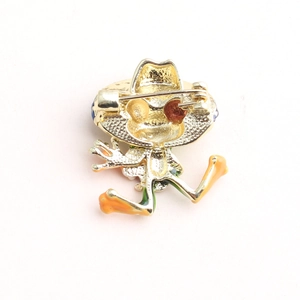 Cartoon frog pin badge with cowboy hat seen from the golden metal back with safety pin
