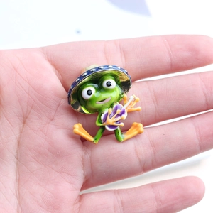 Detail view of a green cartoon frog enamel pin playing a purple guitar on hand
