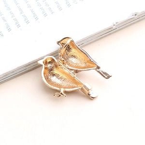 Kreative goldfarbene Vogel-Emaille-Broschen auf einem minimalistischen Buchhintergrund