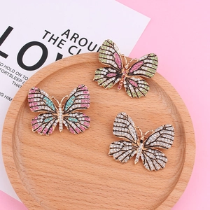Détail de trois broches papillon avec strass colorés sur un plateau en bois