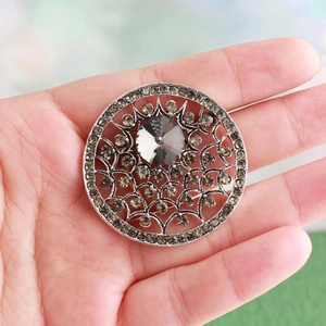 Vue détaillée d'une broche baroque ronde argentée avec strass fumés et gravure creuse