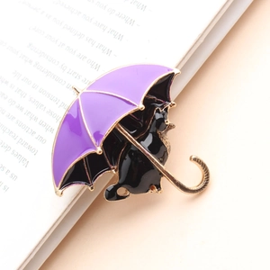Dettaglio macro della spilla smaltata con gatto nero e ombrello viola sul libro