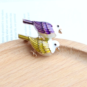 Detailansicht der bunten Emaille-Vogelbrosche auf Holztablett mit Vintage-Papierhintergrund