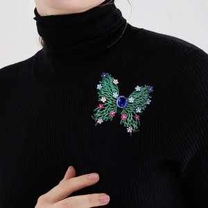Luxury butterfly brooch with green cubic zirconia and blue center stone on black sweater
