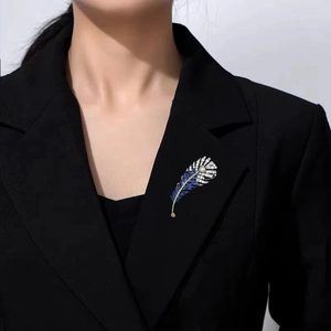 Dettaglio della spilla a piuma con zirconi blu e bianchi su un blazer nero