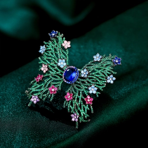Macro detail of luxury butterfly brooch featuring blue center stone and green pavé crystals