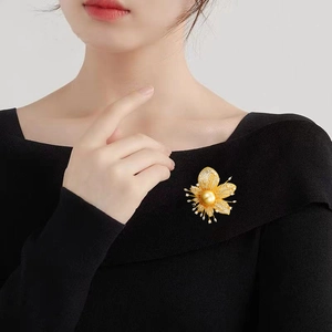 Elegante goldene Blumenbrosche mit Zirkonia und großer Perle auf schwarzer Kleidung getragen