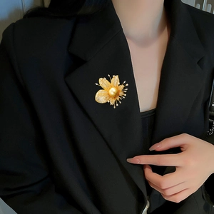 Detailansicht der Luxus-Blatt-Blumenbrosche mit großer Goldperle auf schwarzem Sakko
