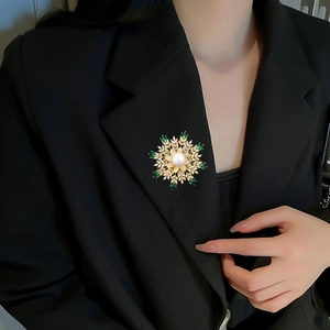 Detailed view of luxury gold snowflake brooch with pearl and green zircon on black blazer