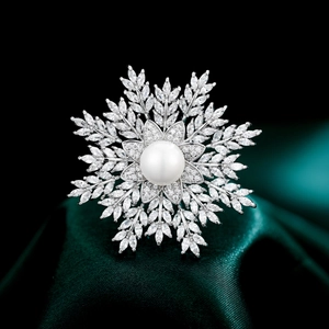 Sparkling snowflake brooch with a central pearl and zircon pavé on green silk background