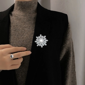 Close-up of snowflake brooch with zircon pavé and white pearl on black blazer lapel