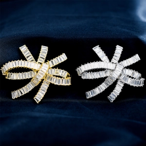 Detailed view of silver and gold bow brooches with baguette-cut zircon on blue silk