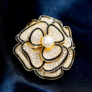 Vista macro della spilla a camelia con strass bianchi e perla centrale su seta blu