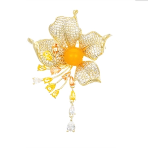 Macro detail of a gold flower brooch featuring orange center stone and zircon tassels