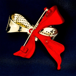 Macro shot of an elegant bow brooch with red enamel and gold-plated details on blue fabric