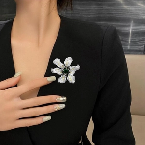 Detailed view of luxury flower brooch with green center stone on black blazer lapel