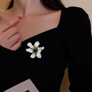 Elegant 3D flower brooch with cubic zirconia and a deep green center stone on black coat