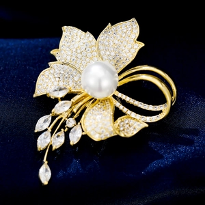 Elegant gold flower brooch with white pearls and sparkling cubic zirconia on blue velvet