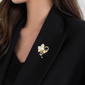 Elegant gold flower brooch with cubic zirconia petals and long pearl tassel on black blazer